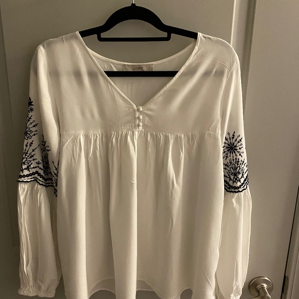 White blouse with navy blue stitching around the arms